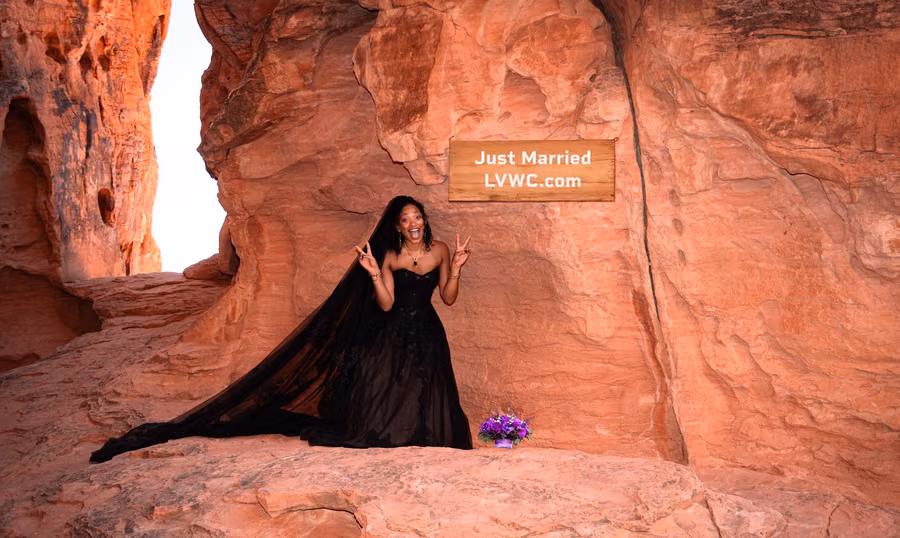 Just married bride celebrating beneath a 'Just Married' sign in a Valley of Fire red rock alcove, Nevada