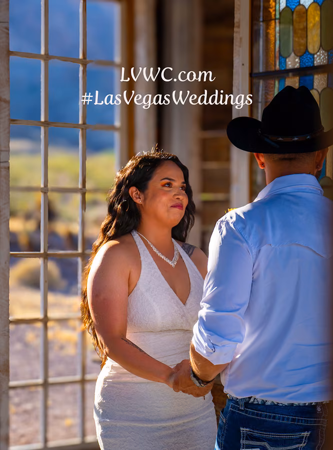 Couple holding hands beside a stained glass window at Nelson Ghost Town, groom in a cowboy hat