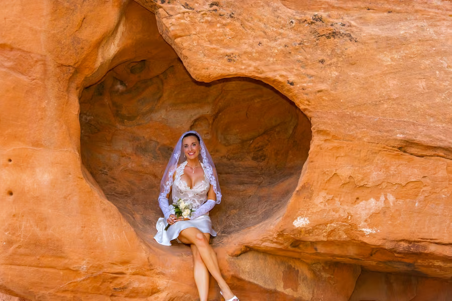 Bride with bouquet seated in a red sandstone alcove at Valley of Fire State Park, Nevada