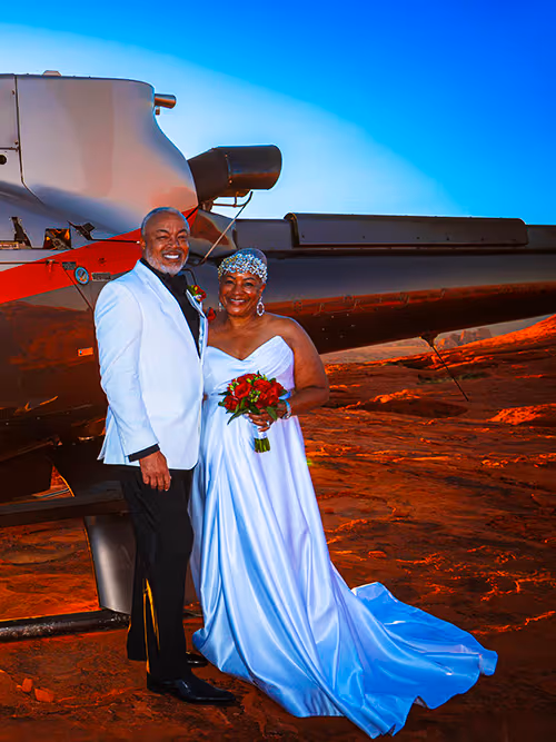 Bride and groom standing beside their helicopter on a red rock landing site at Valley of Fire, Nevada