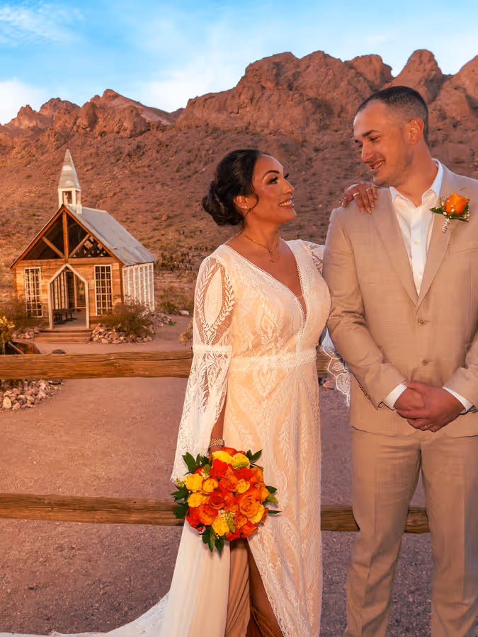 Bride and groom at golden hour above the little white chapel and desert mountains at Nelson Ghost Town, Nevada