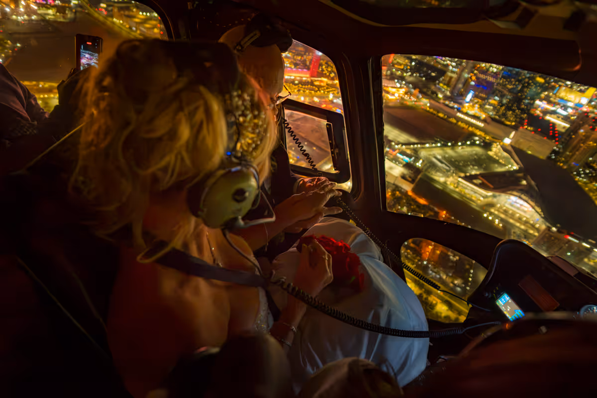 Couple holding hands in the helicopter cabin as the Las Vegas Strip glows below at night